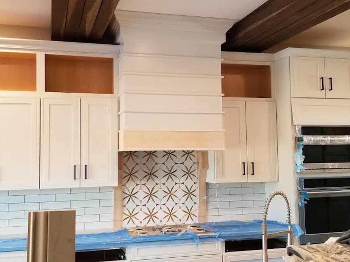 Finished white kitchen cabinetry with patterned tile backsplash and dark wood ceiling beams.